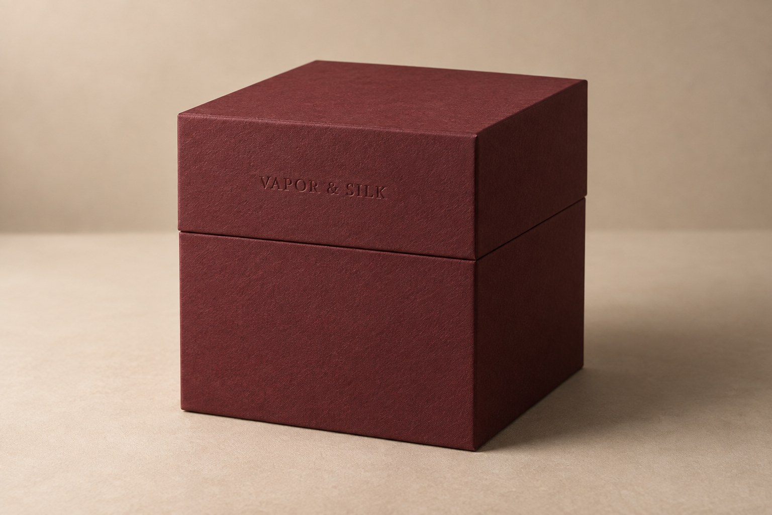 Material study of a closed oxblood rigid box with textured uncoated wrap and a blind-debossed wordmark